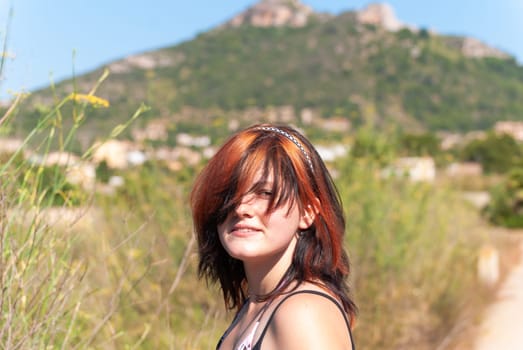 Young woman with orange black hair looking at camera while standing in front of a mountain near cala millor, majorca, spain