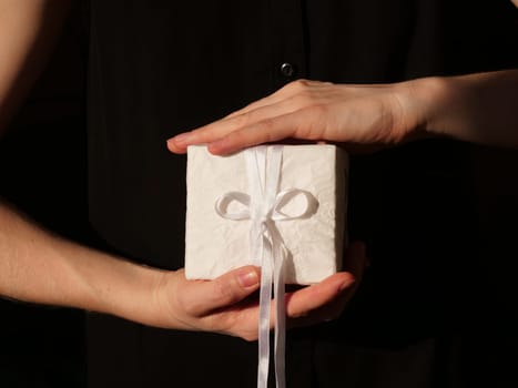Gift in the hands of the birthday girl in white closeup on black background