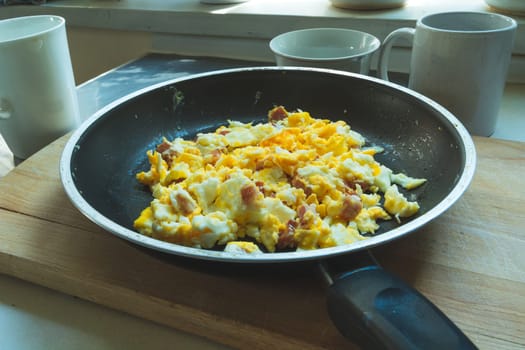 Fresh scrambled eggs with bacon in a pan, homemade food