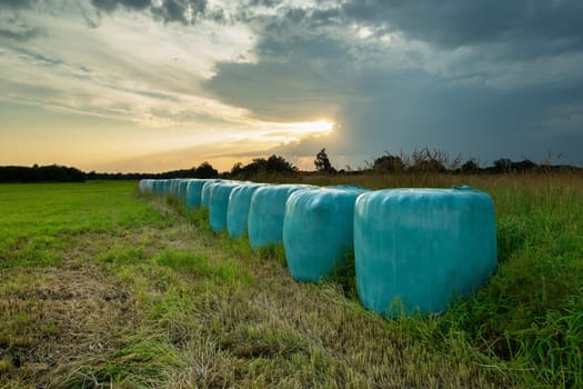 Hay bales in foil and the sunset behind the clouds, Nowiny, Poland