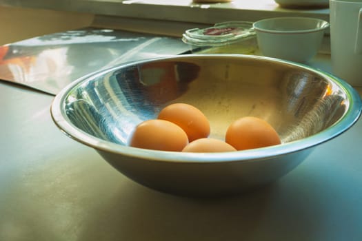 Four chicken eggs in an aluminum bowl on the countertop