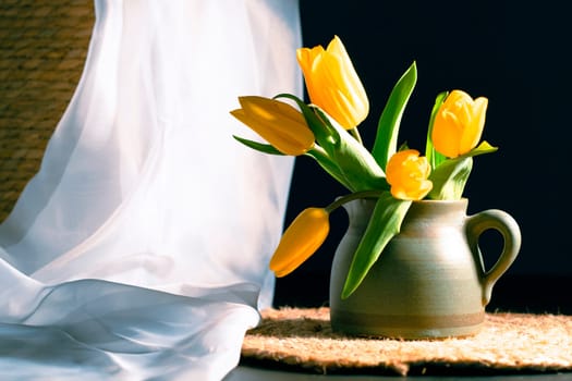 Still life with bouquet of yellow tulip flowers in old vintage jug, in beam of light on dark background.Art photography.