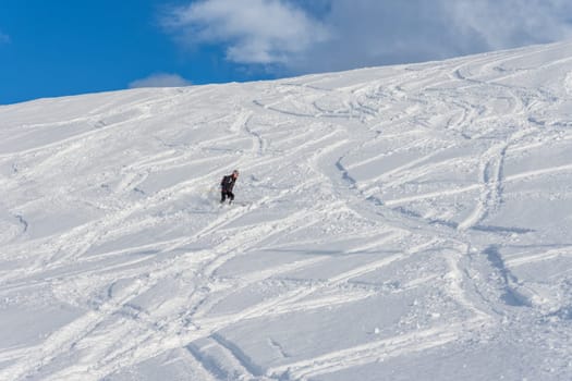 Woman with brown hair, wearing ski wear and a bagpack skiing down a beautiful snow hill with plenty of tracks on the snow, view from the side from far away, stryn norway, horizontal