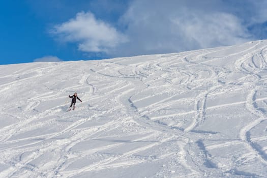 Woman with brown hair, wearing ski wear and a bagpack skiing down a beautiful snow hill with plenty of tracks on the snow, front view from far away, stryn norway, horizontal