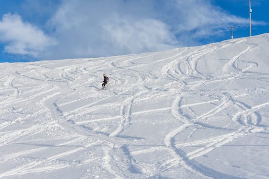 Woman with brown hair, wearing ski wear and a bagpack skiing down a beautiful snow hill with plenty of tracks on the snow, view from the side from far away, stryn norway, horizontal