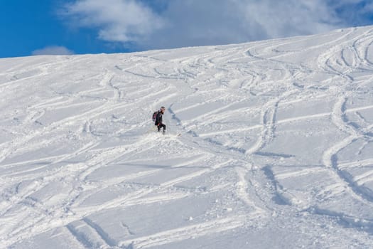 Woman with brown hair, wearing ski wear and a bagpack skiing down a beautiful snow hill with plenty of tracks on the snow, view from the side from far away, stryn norway, horizontal