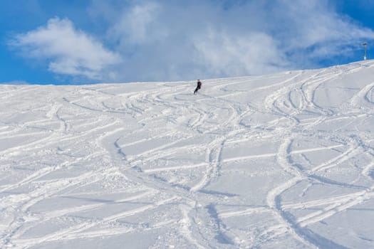 Woman with brown hair, wearing ski wear and a bagpack skiing down a beautiful snow hill with plenty of tracks on the snow, view from the side from far away, stryn norway, horizontal