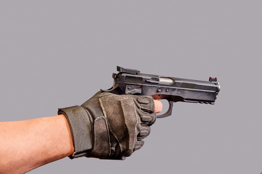 A man's hand holds a black pistol in his hand on a gray background. High quality photo