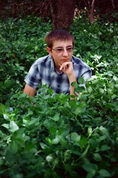 Young man in nature among green plants thinking