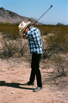 Young boy in natural terrain desert golfing