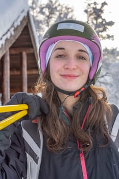 Woman with brown hair smiling, looking at camera, wearing ski wear and a ski helmet, holding ski poles on her right shoulder, close-up, in  skiing stryn, norway