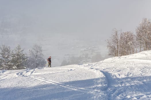 Woman with brown hair, wearing black ski wear and helmet skiing down the top of a mountain, looking back in direction of the camera, rear view, beautiful snow landscape, valley in the distance, fog, horizontal