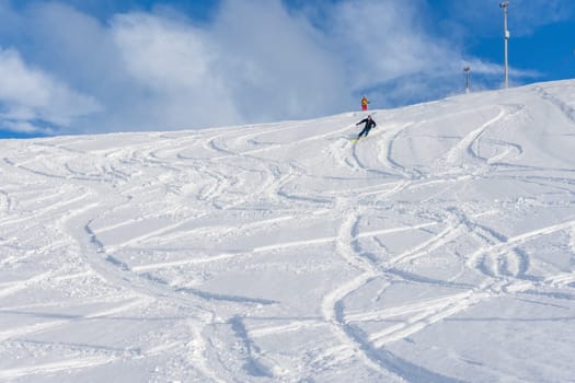 Woman with brown hair, wearing ski wear and a bagpack skiing down a beautiful snow hill with plenty of tracks on the snow, view from the front from the distance, stryn norway, horizontal