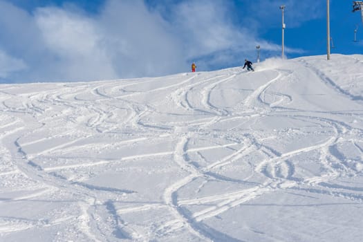 Woman with brown hair, wearing ski wear and a bagpack skiing down a beautiful snow hill with plenty of tracks on the snow, view from the side from far away, stryn norway, horizontal