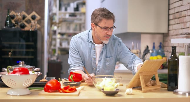 Man cooking in kitchen at home reading recipe on tablet. Healthy eating, diet, cooking application.