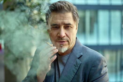 Middle age man smoking cigar outdoor in front of office building, thinking, looking away.