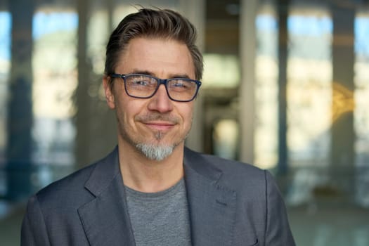 Middle aged confident businessman in business casual in office. Portrait of happy mid adult man in 50s, smiling, looking at camera.