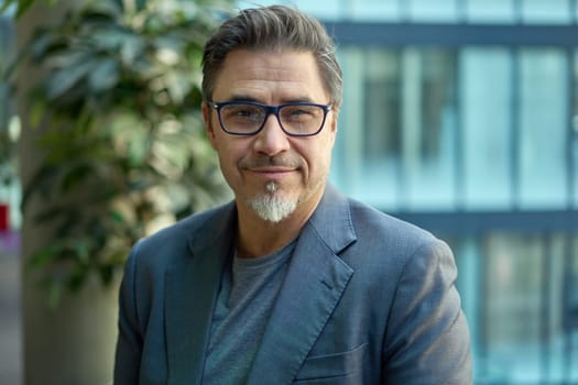Middle aged confident businessman in business casual in office. Portrait of happy mid adult man in 50s, smiling, looking at camera.