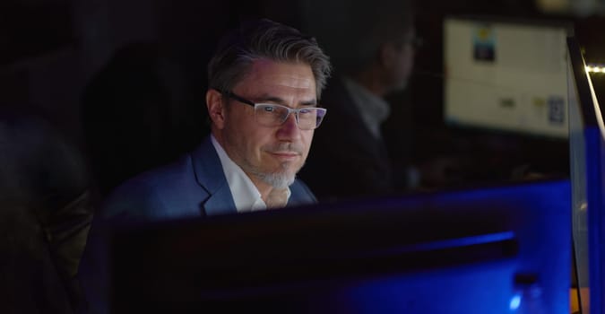 Businessman working with computer at office desk, thinking, smiling. Portrait of happy mid adult man in shirt and jacket, smiling. Bearded, glasses.
