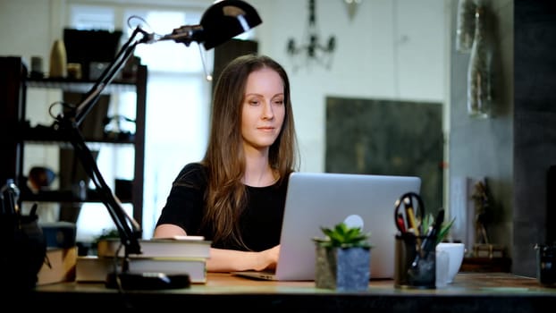Businesswoman using laptop computer managing small business online in home office. Happy, smiling woman. Confident female entrepreneur.