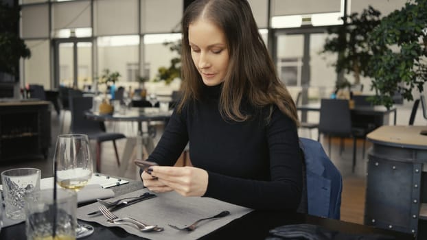 Happy smiling middle age woman using phone sitting in restaurant or cafe.