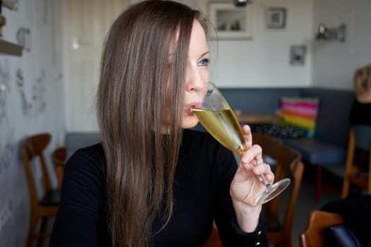 Portrait of a young white woman sitting at table smiling feeling happy and drinking champagne in cafe.