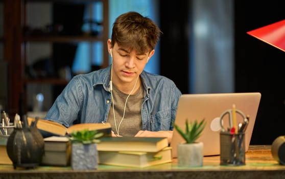 Teenage student learning at home with books and laptop computer. Online school and education, sitting at desk.