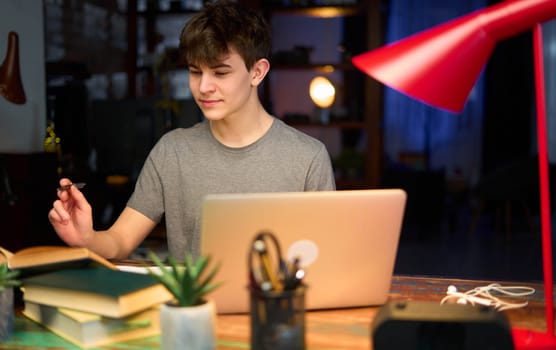 Teenage student learning at home with books and laptop computer. Online school and education, sitting at desk.