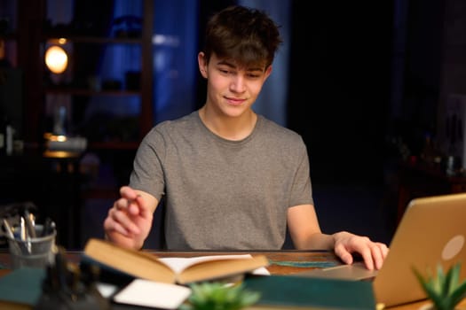 Teenage student learning at home with books and laptop computer. Online school and education, sitting at desk late night