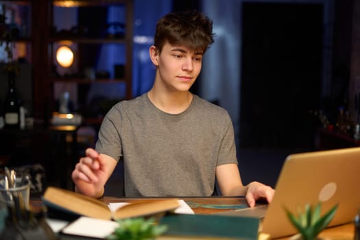 Teenage student learning at home with books and laptop computer. Online school and education, sitting at desk.