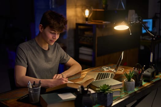 Teenage student learning at home with books and laptop computer. Online school and education, sitting at desk late night