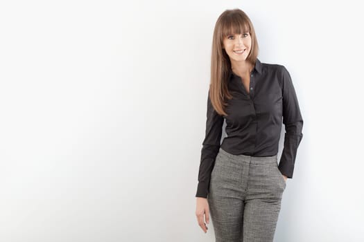 Happy young white businesswoman in business casual standing against gray wall. Copy space for your text.