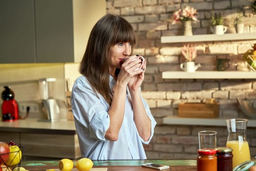 Happy white woman at home drinking coffee at morning in kitchen.