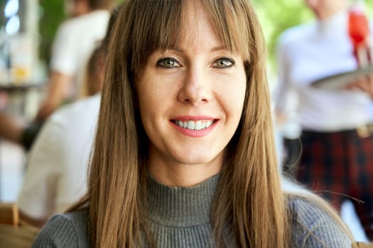 Portrait of attractive happy young woman looking at camera on cafeteria terrace.