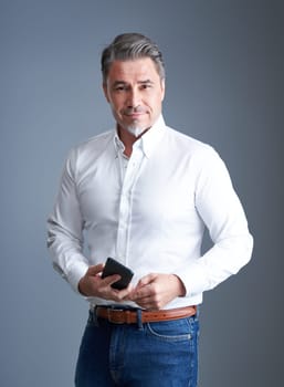 Portrait of older businessman holding phone against gray background.