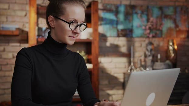 Smart woman in glasses working at home with laptop computer sitting at desk in home office.