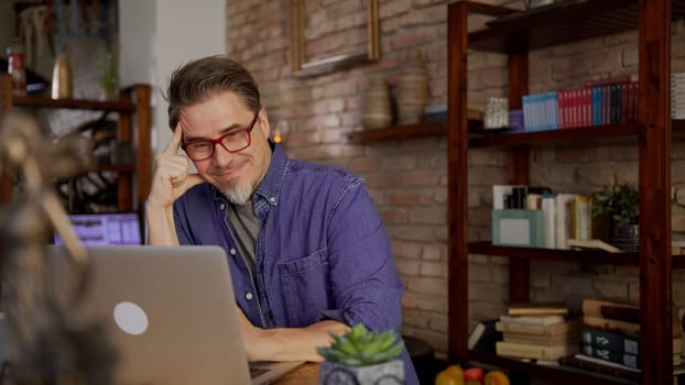 Mature businessman working from home online. Man in 50s sitting at desk browsing internet on laptop computer and teleworking in home office.