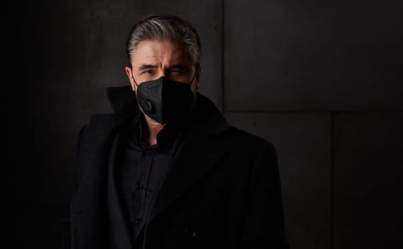 Covid-19 - portrait of older man in 50s with gray hair wearing medical face mask. Dark background copy space.
