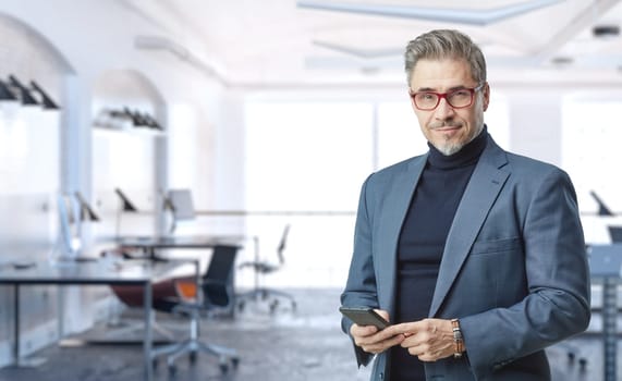 Business portrait - confident businessman in office. Trustworthy older man in his 50s with gray hair wearing glasses and jacket. Copy space.