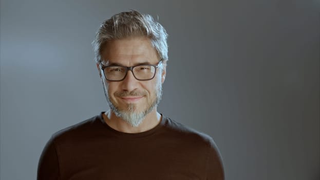 Portrait of happy older white man in glasses on gray background, smiling, copy space.