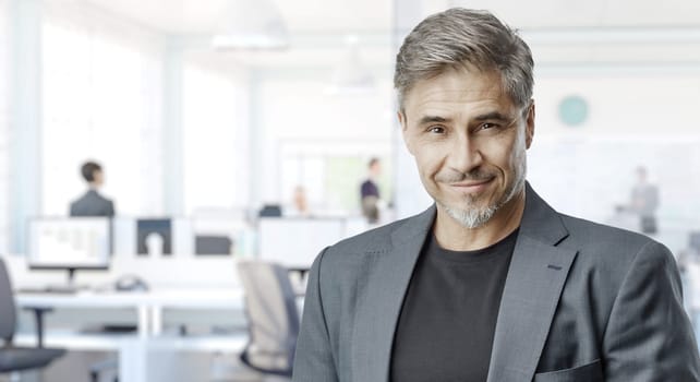 Business portrait - confident businessman in office. Trustworthy older man in his 50s with gray hair. Copy space.