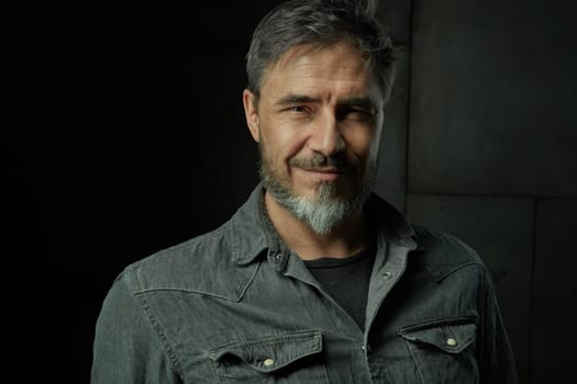 Portrait of casual older man with beard against dark background.
