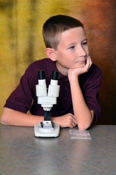 Young boy scientist with microscope examining a sample