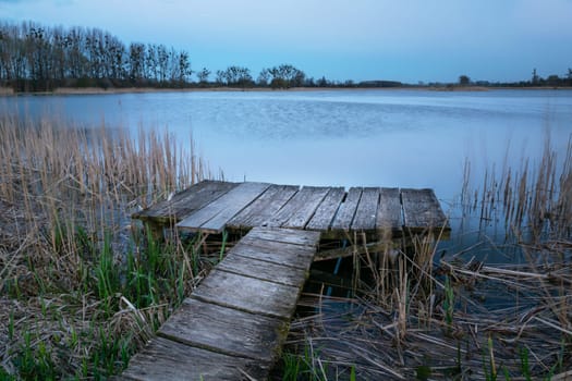 A wooden platform for anglers by the lake shore, evening spring view