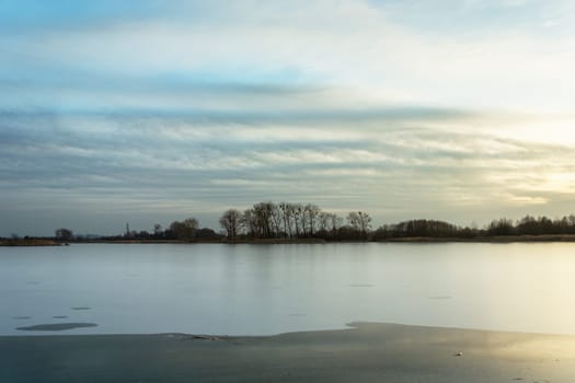 Frozen lake, trees on the shore and clouds, Stankow, Poland