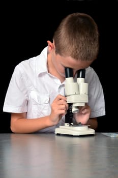 Young boy scientist with microscope examining a sample