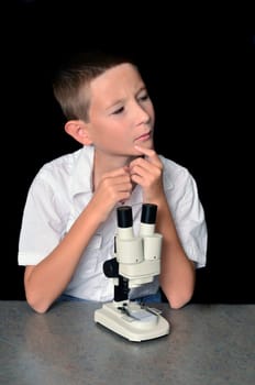 Young boy scientist with microscope examining a sample