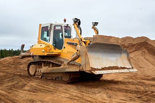 A yellow tractor bulldozer stands in a sand pit. High quality photo
