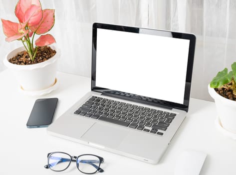 Modern workspace, mock up laptop computer blank white screen, eyeglasses and smartphone white table have potted plants on the desk, Notebook and mobile phone on desktop home office