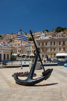 SYMI, Greece - 03 JUNE 2021. A old big Anchor sculpture on Symi town promenade on the pictorial port of Symi island in Greece. Dodecanese.